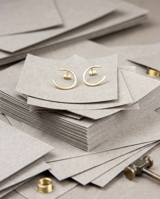 Pendientes Sumatra sencillos dorados sobre cartones grises en el taller, junto a herramientas